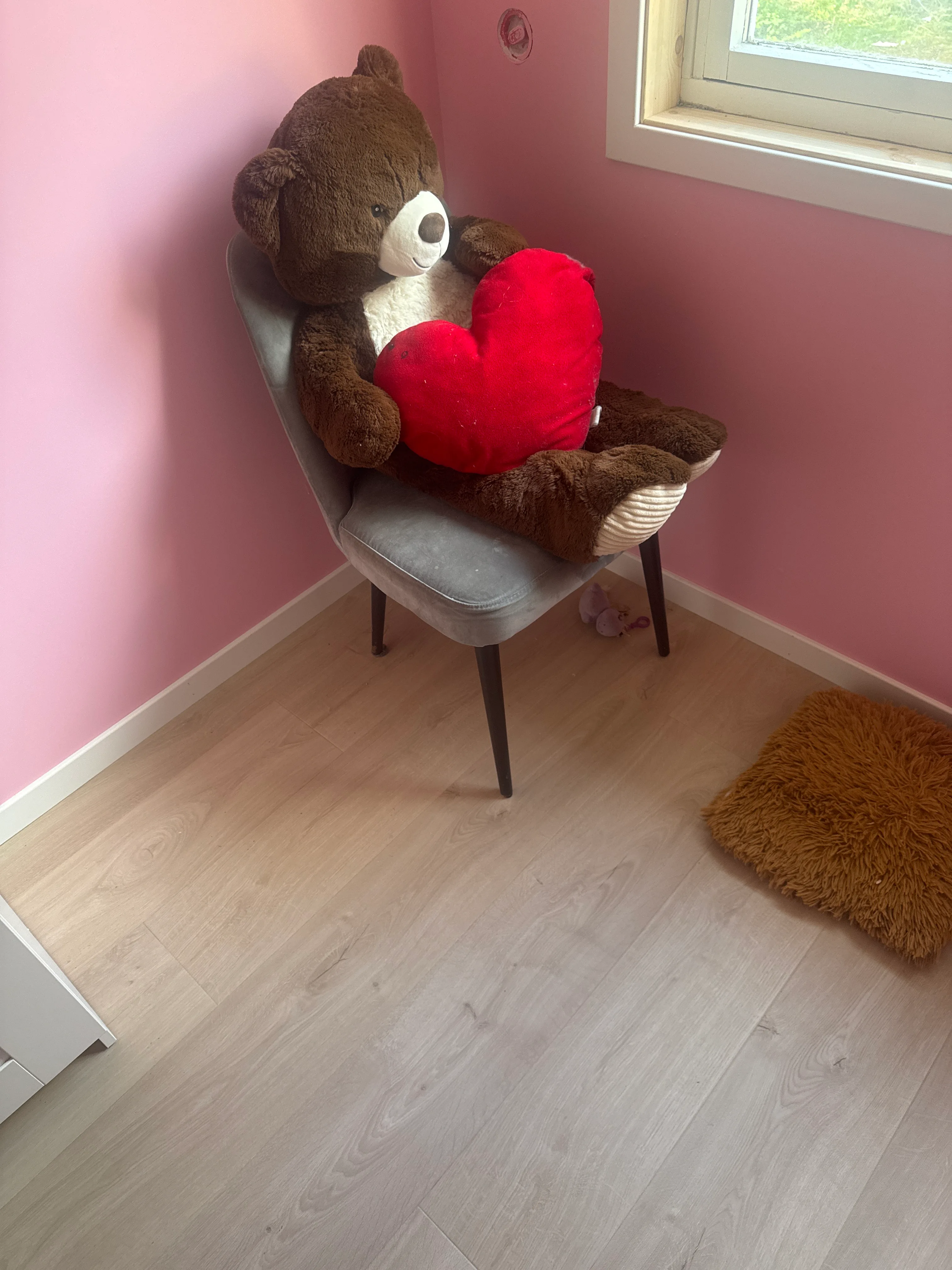 Brown teddy bear holding red heart on chair