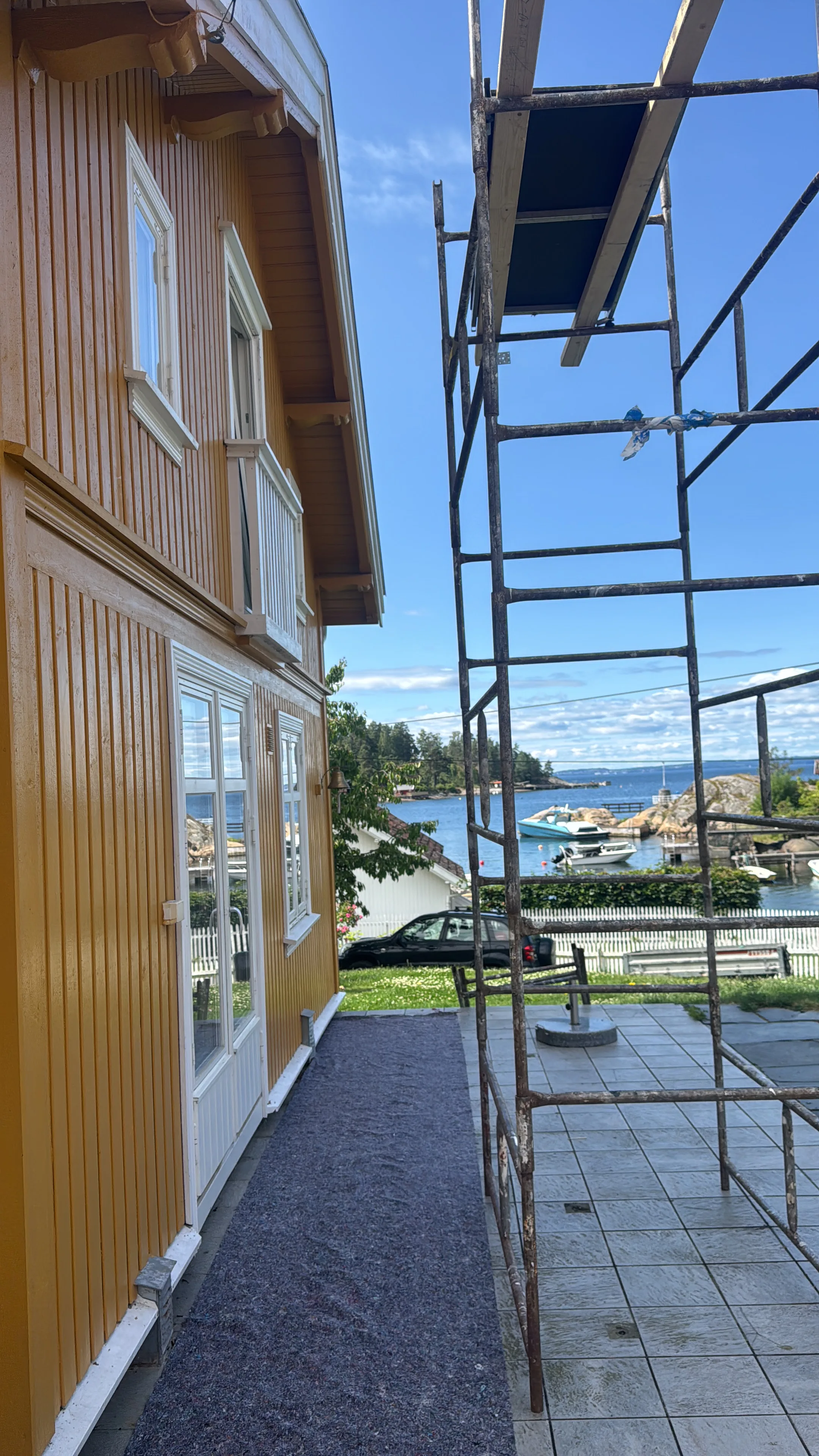 Huset i bakgrunnen med ny malt fasade, stillas på siden for fasaderenovering